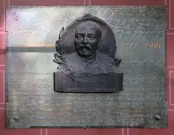 plaque en marbre vert sur laquelle est apposé le portrait en bronze de Lenoir ;&nbsp;en lettres dorées figure l’inscription suivante : Étienne Lenoir (portrait) 1822 - 1900  Inventer du premier moteur à gaz industriel 1860  Plaque commémorative érigée par souscription sur  l'initiative de la Chambre Syndicale de l’Industrie des moteurs  à gaz, à pétrole et des gazogènes le 16 décembre 1912 Monsieur Fernand David, ministre du commerce et de l’Industrie (J. Malet)