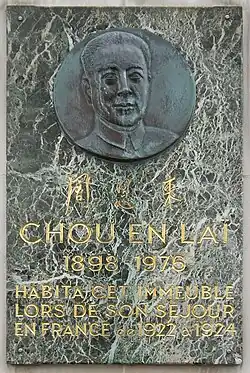 Photographie d'une plaque de marbre portant en haut un buste sculpté sur un médaillon métallique, au centre trois sinogrammes et en bas le texte suivant : « Chou En Laï 1898-1976 habitat cet immeuble lors de son séjour en France de 1922 à 1924 ».