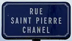 Panneau rectangulaire bleu avec liseré blanc, indiquant, en majuscules blanches, "rue Saint-Pierre Chanel"