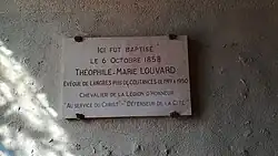 Une plaque commémorative est vissée sur un mur ; on y lit : Ici fut baptisé le 6 octobre 1858 Théophile-Marie Louvard Évêque de Langres puis de Coutances de 1919 A 1950 Chevalier de la Légion d'Honneur "Au service du Christ" - "Défenseur de la Cité"