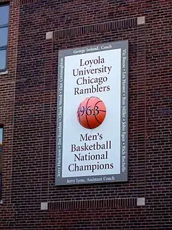 Sur un mur en briques rouges, un panneau blanc avec au centre un ballon marqué 1963, année du titre de l'équipe masculine des Ramblers de Loyola.
