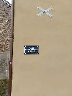 Photographie en couleurs d'une plaque de rue bleue sur un mur beige.