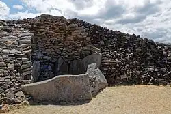 Polygone dessiné par de gigantesques pierres debout, dont une partie est hors du cairn. Mais elles ne sont pas couvertes d'une table. À l'arrière, on voit les maigres restes de la voûte en encorbellement.