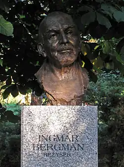 Photographie d'un buste entouré d'arbustes.