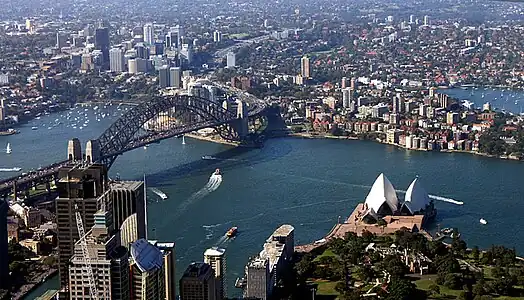 Vue aérienne du port de Sydney, avec l'opéra (qui s'avance comme un promontoire sur l'eau) et le pont.