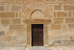 Photographie de la porte du minaret, encadrée d'un linteau et de pieds-droits sculptés d'origine antique. Elle est surmontée d'un arc de décharge en fer à cheval.