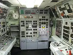 Des panneaux avec des écrans analogiques et des commandes tapissent les parois d'une pièce rectangulaire