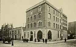 Photographie en noir et blanc de 1909 représentant l'immeuble où siège l'association. A gauche, une charrette tirée par un cheval.