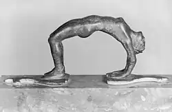 Poignée en métal dont la base est constituée des pieds et des mains d'une femme en train de s'arc-bouter, ventre vers le haut.