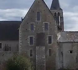 Photographie en couleurs d'un mur flanqué d'un contrefort, percé de sept fenêtres et terminé par une maçonnerie triangulaire, le tout encadré par des bâtiments à toits pentus, la flêche d'un clocher visible en arrière-plan.
