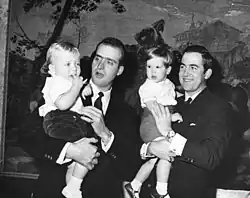 Photo en noir et blanc montrant deux hommes d'une trentaine d'années tenant deux petits garçons dans leurs bras.