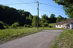 Une petite colline boisée sur la gauche et une maison simple à droite.