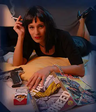 Une femme brune allongée sur le ventre les jambes à demi-repliées et fumant une cigarette, avec un pistolet et un magazine posé devant elle, parodiant Uma Thurman sur l'affiche du film.