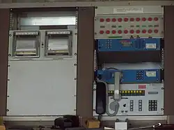 Pupitre de commande, bâtiment principal ; la rangée de boutons rouges servait à positionner les antennes en survie ; à gauche des boutons : 2 anémomètres, pour les antennes (2008). Les 2 boitiers bleus sont des téléphones Inmarsat.