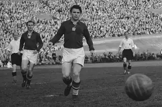 Photographie en noir et blanc de deux joueurs en maillot foncé, devant un ballon.