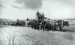 Photo en noir et blanc d'un convoi de chariots tirés par des bœufs avec des hommes en uniforme et en civil dans une plaine