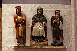 Photographie d'un ensemble de trois statuettes polychromes représentant un homme assis entre deux hommes debout, l'un richement vêtu et l'autre pauvre.