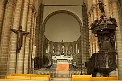 Photographie d'un chœur d'église avec un crucifix vêtu suspendu au pilier gauche et une chaire à prêcher sur le pilier droit