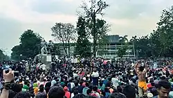 Une foule, vue de derrière, en train de manifester face à un bâtiment.