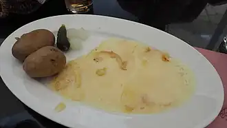 Raclette servie avec des pommes de terres, des cornichons et des petits oignons.