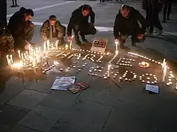 Des personnes s'asseyent le temps d'un instant pour mettre en place des bougies commémoratives traçant un Charlie Hebdo