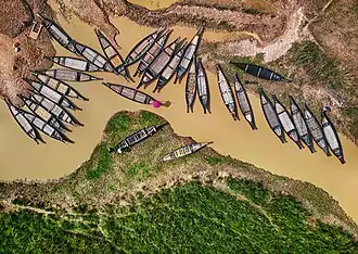 Bateaux ressemblant à des pirogues sur le lit d'une rivière accostés à un quai ou sur la berge. Il occupe pratiquement tout un coté de la rivière.