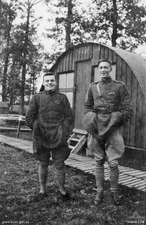 Deux hommes en uniforme militaire se tiennent côte à côte. L'homme de gauche est petit et trapu, celui de droite est grand et mince. À l'arrière-plan se trouve une cabane.