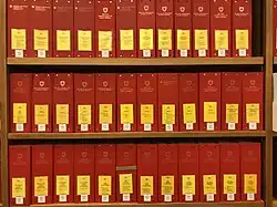 Photographie de 36 classeurs rouges avec étiquette jaune sur une étagère