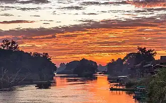 Nuages rouges au-dessus des berges du Mékong avec des habitations et des pirogues au lever du soleil à Don Det.
