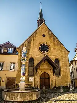 Façade du temple protestant de la commune de Boudry, en Suisse, avec au premier plan une fontaine surmontée d'une statue allégorique de la Justice.