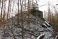 Photographie récente en couleurs d'une colline artificielle conique portant à son sommet une infrastructure bétonnée. L'ensemble est envahi par la forêt.
