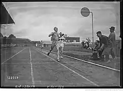 Photographie en noir et blanc d'un homme en tenue foncée de l'équipe de France portant le dossard no 22. Il s'agit de René Wiriath. Il devance un homme en tenue blanche, représentant l'équipe d'Allemagne, portant le dossard no 15