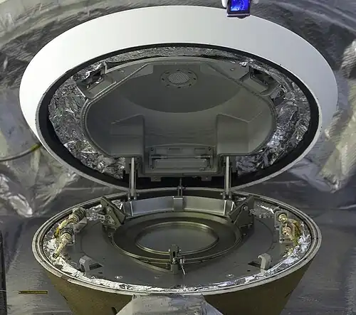 La porte de la capsule entrouverte permet d'apercevoir le logement qui doit recevoir la tête du système de prélèvement TAGSAM.