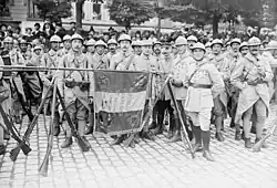 Soldats autour d'un drapeau tricolore. La hampe du drapeau est posée horizontalement sur deux trépieds de fusils.