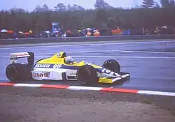 Photo d'une monoplace jaune, blanche et bleue, vue de côté droit, sur une piste détrempée.
