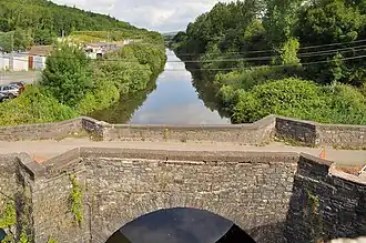 Un pont en pierre enjambant un cours d'eau aux rives arborées.
