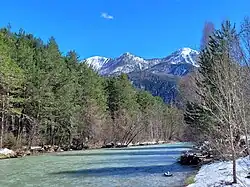 Photo montrant une rivière ancadrée par des arbres avec en arrière-plan des montagnes enneigées.