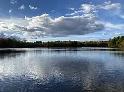 Photographie d'une rivière calme. Une forêt aux couleurs d'automne apparaît à l'arrière-plan.