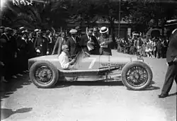 Photo d'un homme prenant la pause au volant de sa voiture, cernée par la foule.