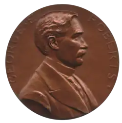 Médaille de couleur bronze, montrant le buste de profil d'un homme moustachu au cheveux courts et comprenant l'inscription George E. Roberts.