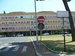 Une longue barre d'immeubles à la façade décrépie. La rue porte le nom de l'olympiade.