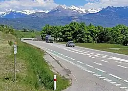Photo montrant une route à deux voies avec des véhicules et en arrière-plan la montagne.