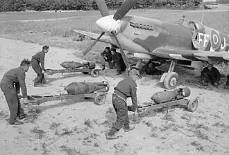 Photographie en noir et blanc de trois hommes installant des obus sous un avion.