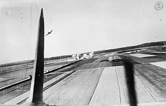 Photo aérienne en noir et blanc montrant des colonnes de fumées vues de loin et, au premier plan, la queue d'un avion..