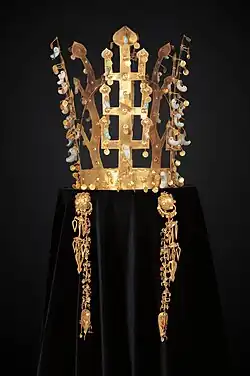 Couronne, daegwan, faite de bandeaux en or en forme d'arbres dressés aux feuilles d'or et pendentifs de jade, magatama (en forme de virgule). Photographie de face, sur fond sombre, la couronne étant posée sur un velours noir.