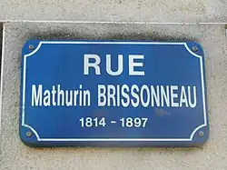 Plaque rectangulaire indiquant «&nbsp;rue Mathurin Brissonneau 1814-1897&nbsp;» en blanc sur fond bleu.