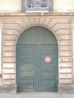 Portail d'immeuble en pierre, avec une grande porte verte en bois.