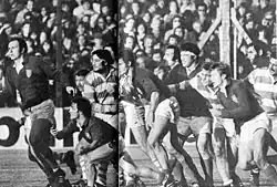 Photographie en noir et blanc. Gros plan sur une action de jeu où un joueur extrait le ballon d'un regroupement et fait une passe vers sa gauche.