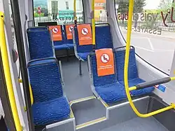 Photographie en couleurs de l’intérieur d’un minibus avec des sièges bleus, condamnés par un écriteau orange pour une partie d'entre eux.