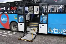 Photographie en couleurs d’un autocar bleu et noir avec un monte-charge pour les UFR sorti, et les portes ouvertes.